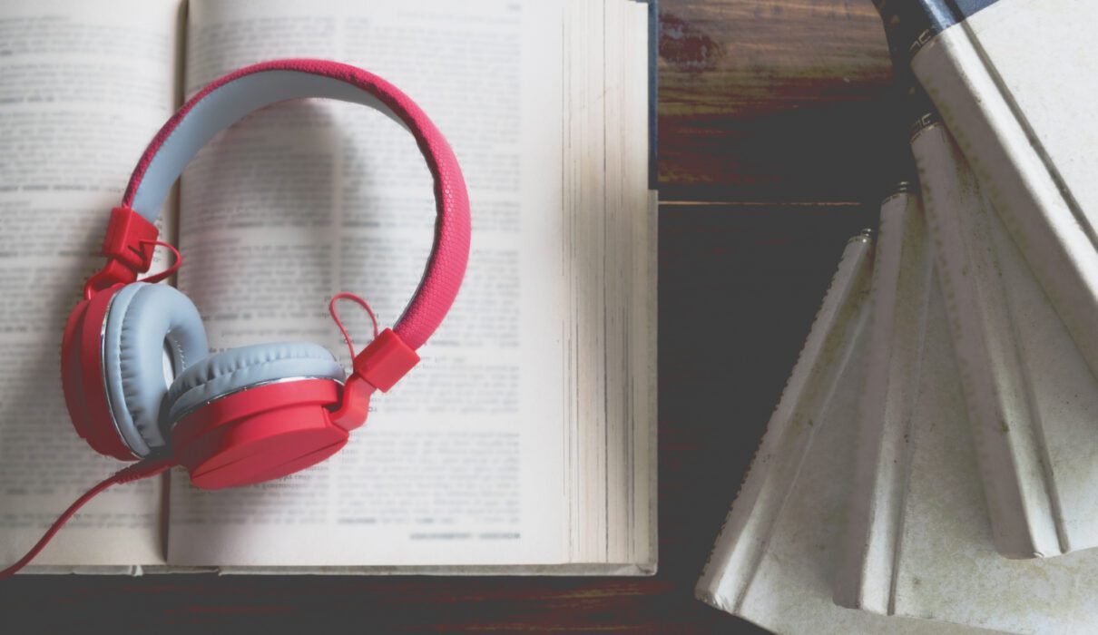 visuel en ambiance douce et feutrée montrant un casque audio posé sur un livre ouvert, sur une table en bois avec une tasse de café, éclairage tamisé type fin de journée