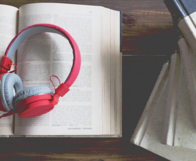 visuel en ambiance douce et feutrée montrant un casque audio posé sur un livre ouvert, sur une table en bois avec une tasse de café, éclairage tamisé type fin de journée