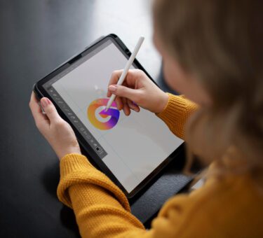une jeune artiste en train de créer sur une tablette graphique ou dans un environnement immersif, avec une projection ou une œuvre digitale colorée en arrière-plan