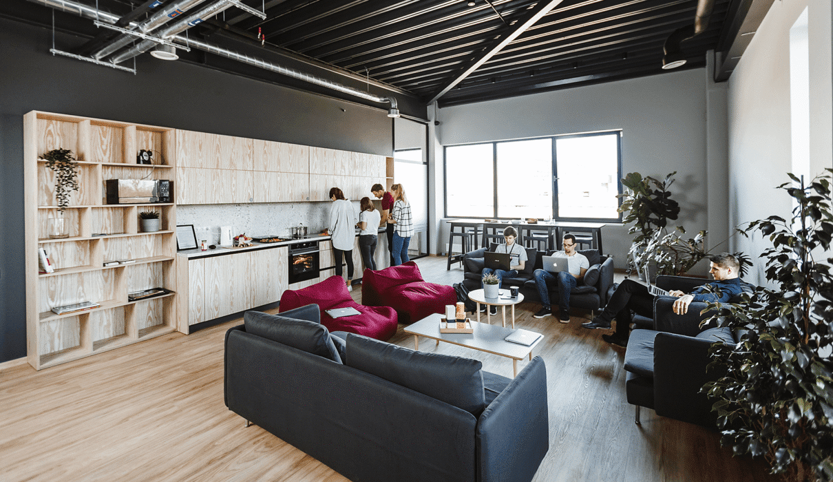 Un grand loft lumineux en centre-ville, avec murs en briques, espace de travail partagé rempli de toiles, ordinateurs portables et imprimantes 3D, et plusieurs jeunes créateurs en pleine discussion autour d’une table