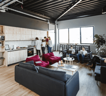 Un grand loft lumineux en centre-ville, avec murs en briques, espace de travail partagé rempli de toiles, ordinateurs portables et imprimantes 3D, et plusieurs jeunes créateurs en pleine discussion autour d’une table