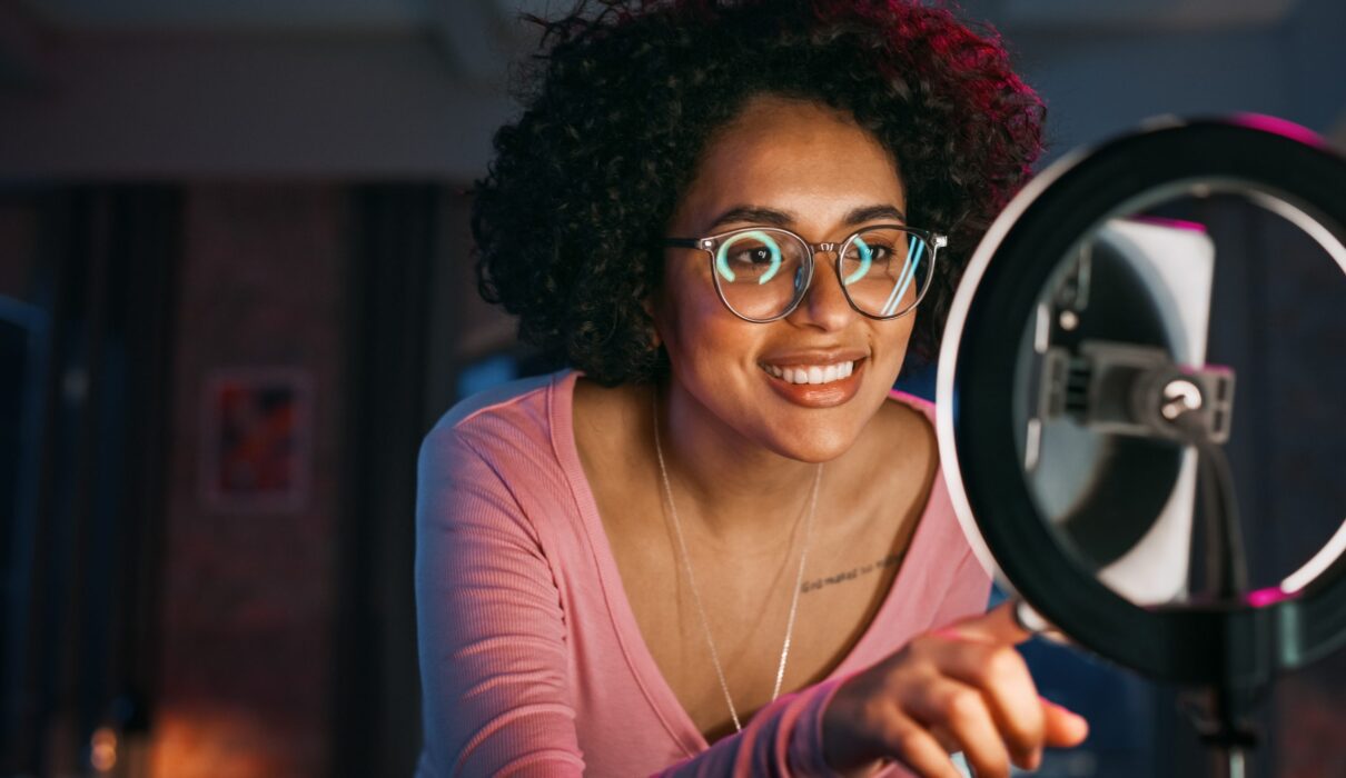 photo en lumière naturelle d’un micro-influenceur en train de créer du contenu chez lui, smartphone à la main, avec un café et un produit sur une petite table, ambiance cosy et spontanée