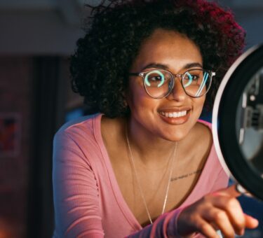 photo en lumière naturelle d’un micro-influenceur en train de créer du contenu chez lui, smartphone à la main, avec un café et un produit sur une petite table, ambiance cosy et spontanée