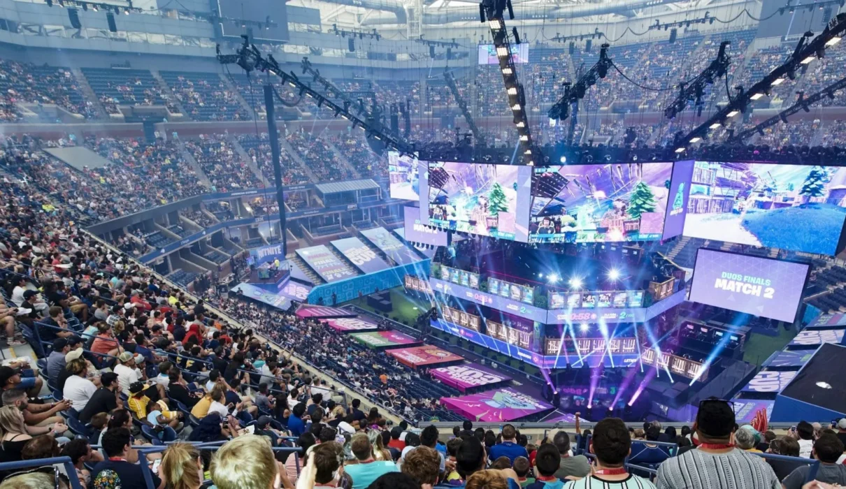 scène d’e-sport dynamique montrant des joueurs sur scène avec des écrans géants, des fans en live, et des graphiques de données et logos de sponsors flottants, symbolisant l’intersection culture, business et technologie