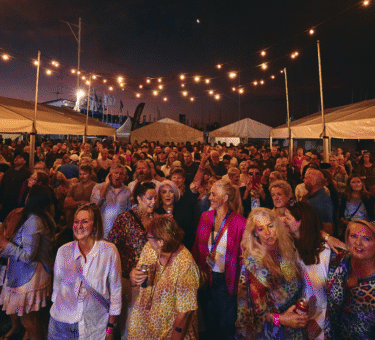 foule de festivaliers stylés sous un ciel coloré, avec des tenues audacieuses et des stands de marques, capturant l’énergie, la créativité et le côté commercial du street style