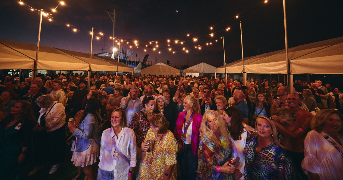 foule de festivaliers stylés sous un ciel coloré, avec des tenues audacieuses et des stands de marques, capturant l’énergie, la créativité et le côté commercial du street style